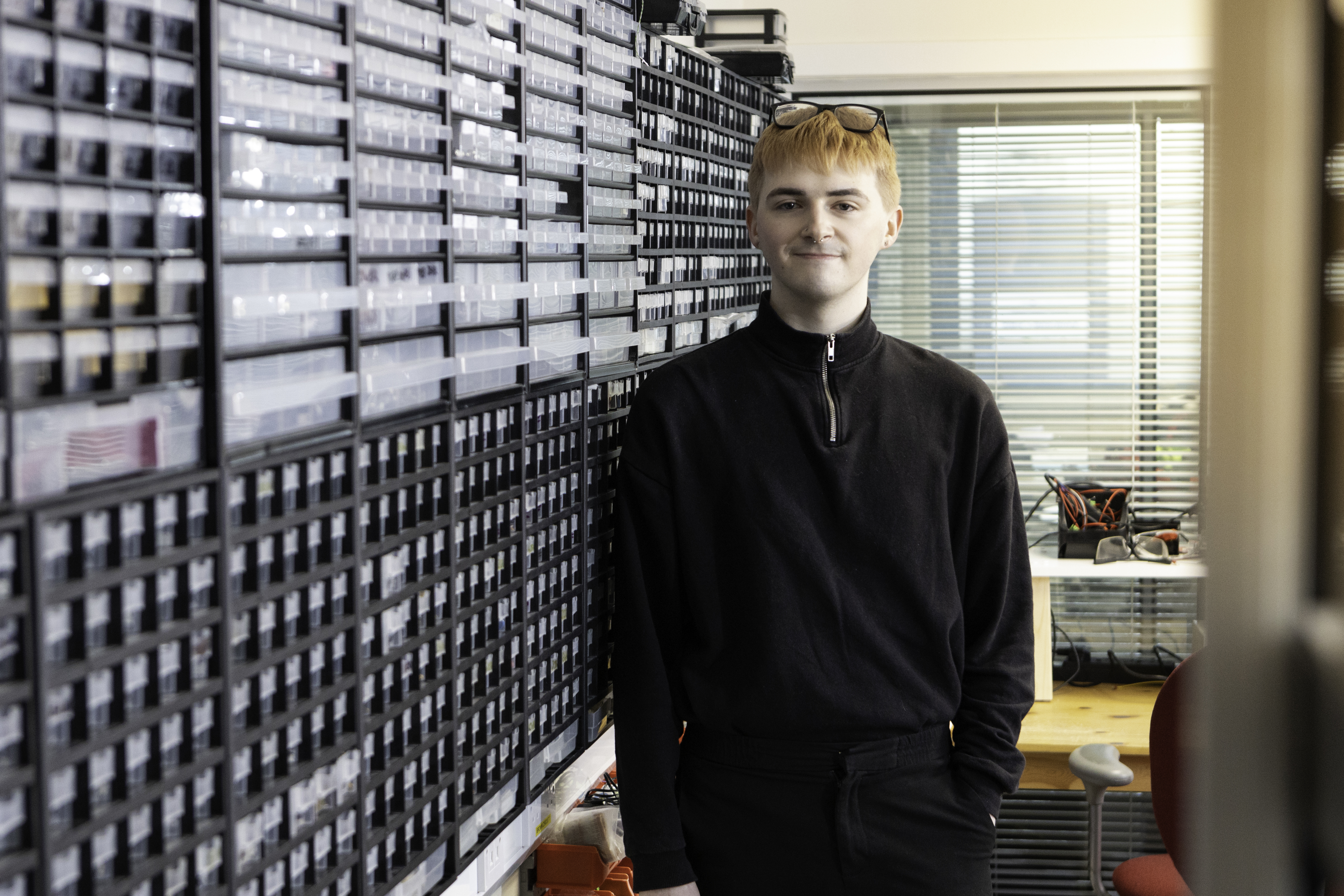 Alan in a black work fleece stands next to rows of small storage for parts