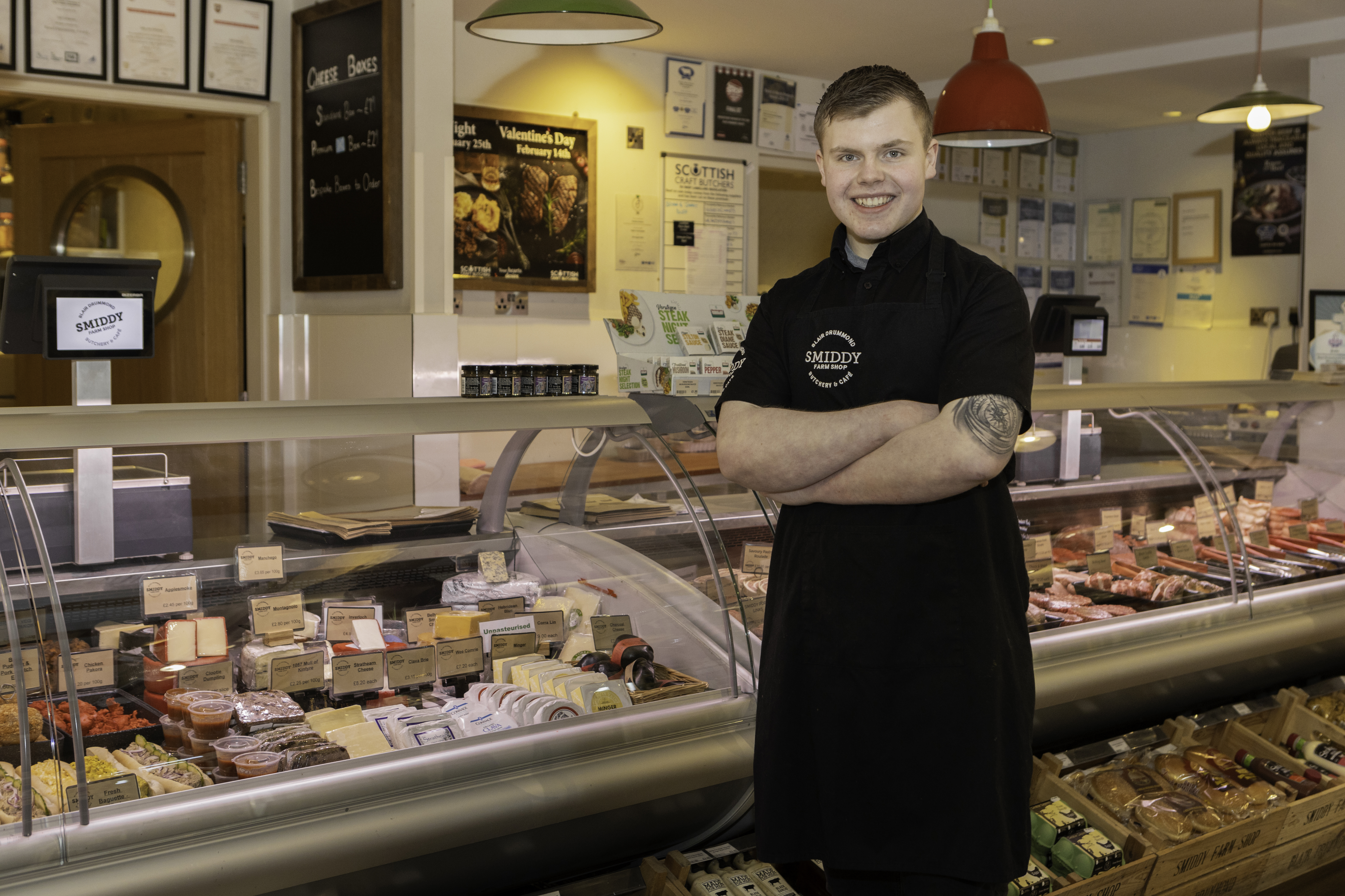 Marc smiles at the camera in front of the counter at the butcher's shop where he works